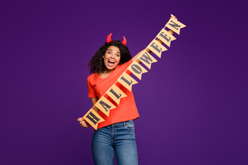 Photo of cheerful positive nice charming cute overjoyed girl holding flags with halloween wirtten on wearing jeans denim orange t-shirt expressing emotions on face isolated purple bright color