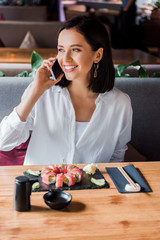 happy woman talking on smartphone in sushi bar