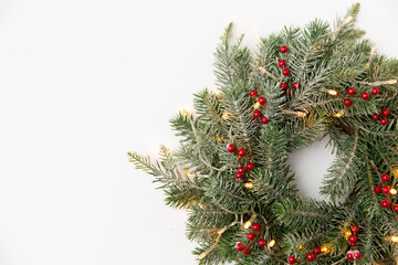 winter holidays, new year and decorations concept - wreath of fir branches with red berries and garland lights on white background