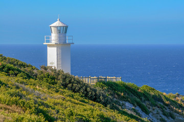 Fototapeta na wymiar White lighthouse against blue sky and ocean