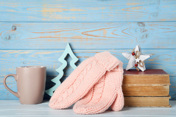 Knitted mittens with books, decorative fir tree and cup on blue wooden background