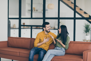 Photo of funny guy and lady having fun best weekend sharing news just moved to rent penthouse sitting sofa in modern flat indoors wear casual clothes