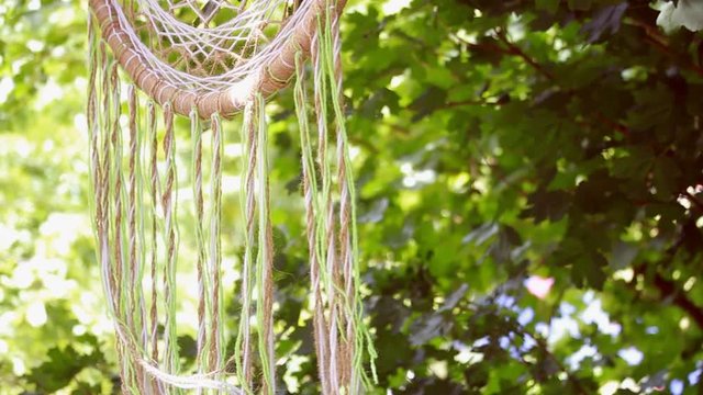 Close-up of a multi-colored hand-woven macrame dreamcatcher hanging on a branch in the park