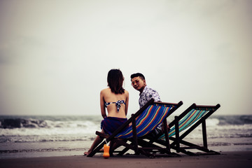 Couple Sitting On Chair At Beach Against Sky