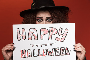 Image of frightening witch girl in hat holding halloween text board