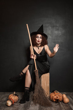 Full length image of young witch girl in halloween costume holding broom