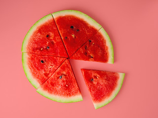 Slices of fresh red delicious watermelon are laid out in a circle on a colored background.