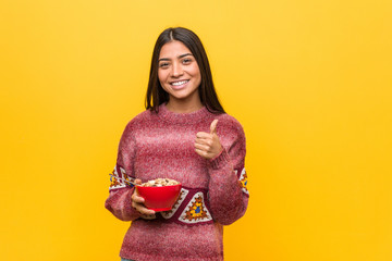 Young arab woman holding a cereal bowl smiling and raising thumb up