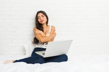 Young arab woman working with her laptop on the bed hugs, smiling carefree and happy.