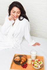 Young hispanic woman having breakfast on the bed