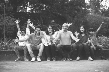Indian Family enjoying Picnic - Multi generation of asian family sitting over or near small wall in park, outdoor. selective focus