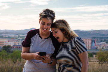 Lesbian couple is having fun with a smartphone in a meadow