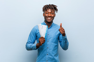 Young rasta black man holding an air tickets smiling and raising thumb up