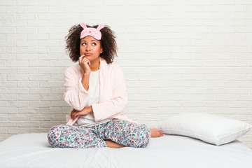 Young african american woman in the bed wearing pijama looking sideways with doubtful and skeptical expression.