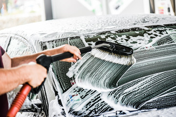 Man cleaning a car with brush and water.  Detal of washing a vehicle using a foam at touch less...