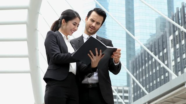 group of two happy businessman and businesswoman discussing with paper report together in modern city  outdoors. coworker meeting . manager appreciation secretary .consulting . jop. work. successful