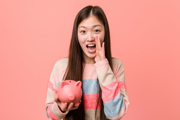 Young asian woman holding a piggy bank shouting excited to front.