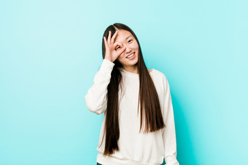 Fototapeta premium Young pretty chinese woman excited keeping ok gesture on eye.