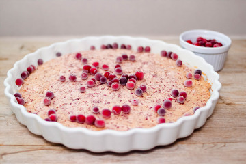 Cake or baked pudding of cottage cheese with red bilberry on white baking dish on wooden background