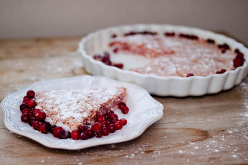 Cake or baked pudding of cottage cheese with red bilberry on white baking dish on wooden background