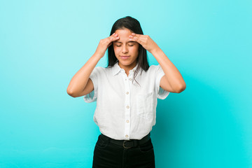 Young hispanic cool woman against a blue wall touching temples and having headache.