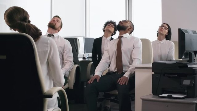Group of diverse businesspeople sitting on office chairs with closed eyes and doing relaxing exercises together