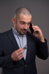 Thoughtful entrepreneur talking on mobile phone while keeping his spectacles rim at his chin