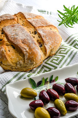 Freshly baked olive bread ready for slicing with a tray of black and green olives 