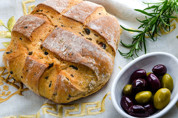 Olive bread together with a dish of black and green olives and a sprig of rosemary. 