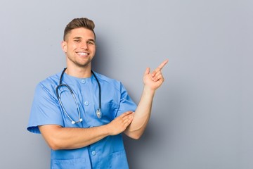 Young nurse man smiling cheerfully pointing with forefinger away.