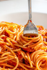 fork close-up wrapped in Italian spaghetti pasta in white plate with ketchup sauce, vertical image