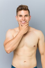 Young caucasian fitness man shirtless touching his chin.