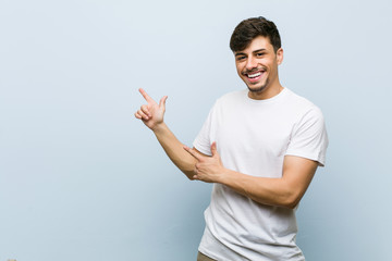Young caucasian man wearing a white tshirt pointing with forefingers to a copy space, expressing excitement and desire.