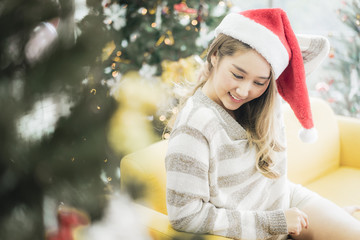 Celebration party of Asian cheerful attractive young woman in Santa Claus hat sitting on yellow sofa happy and funny concept. In 2020 New year holiday.