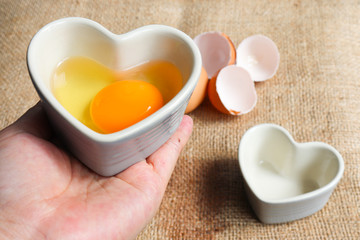 Raw freshness  Egg yolk of chicken  organic  uncooked with eggshell  in Heart shaped ceramic container put on hand of women  concept close up soft focus