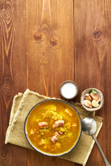 Winter hot soup with chopped green peas, pork, bacon, smoked on dark brown wooden table. Delicious appetizing fat rich soup.