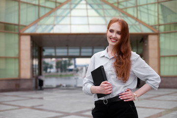 Happy young redhead businesswoman standing at office building