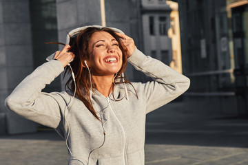 Young woman in gray hoodie enjoys music via earphones on the street