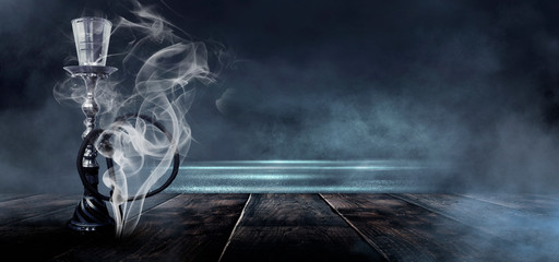 Hookah with smoke on a wooden tabletop. Dark room, blue neon, smoke.