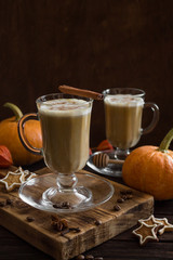 Spicy pumpkin latte in glass Cup on wooden background. Pumpkins, cookies, cinnamon, cloves and coffee. Autumn mood. Side view, copy space. Dark photo