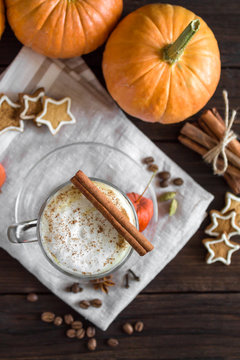 Spicy pumpkin latte in glass Cup on wooden background. Pumpkins, cookies, cinnamon, cloves and coffee. Autumn mood. Top view, copy space. Dark photo. Selective focus