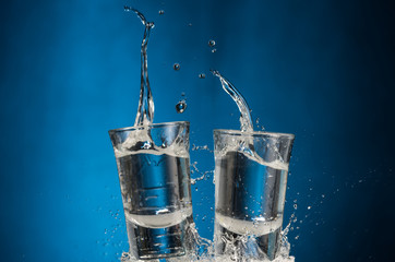 falling glasses with vodka and spray on a blue background