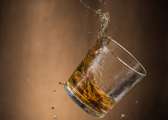 falling glass with whiskey and spray on a brown background