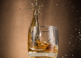 falling glass with whiskey and spray on a brown background