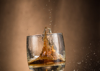 falling glass with whiskey and spray on a brown background