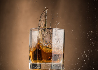 falling glass with whiskey and spray on a brown background