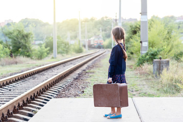 Beautiful charming little girl with pigtails waiting for train at station dressed dark blue dress...