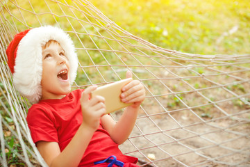 Happy excited child boy in Santa hat lying in hammock. Family vacation and Christmas holidays....