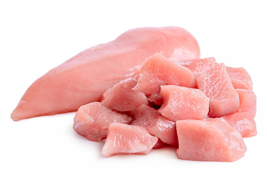 A pile of cut up uncooked boned chicken breast next to whole chicken breast isolated on white.