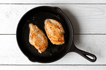 Two whole chicken breasts roasting in cast iron pan isolated on white. Top view. © Moving Moment